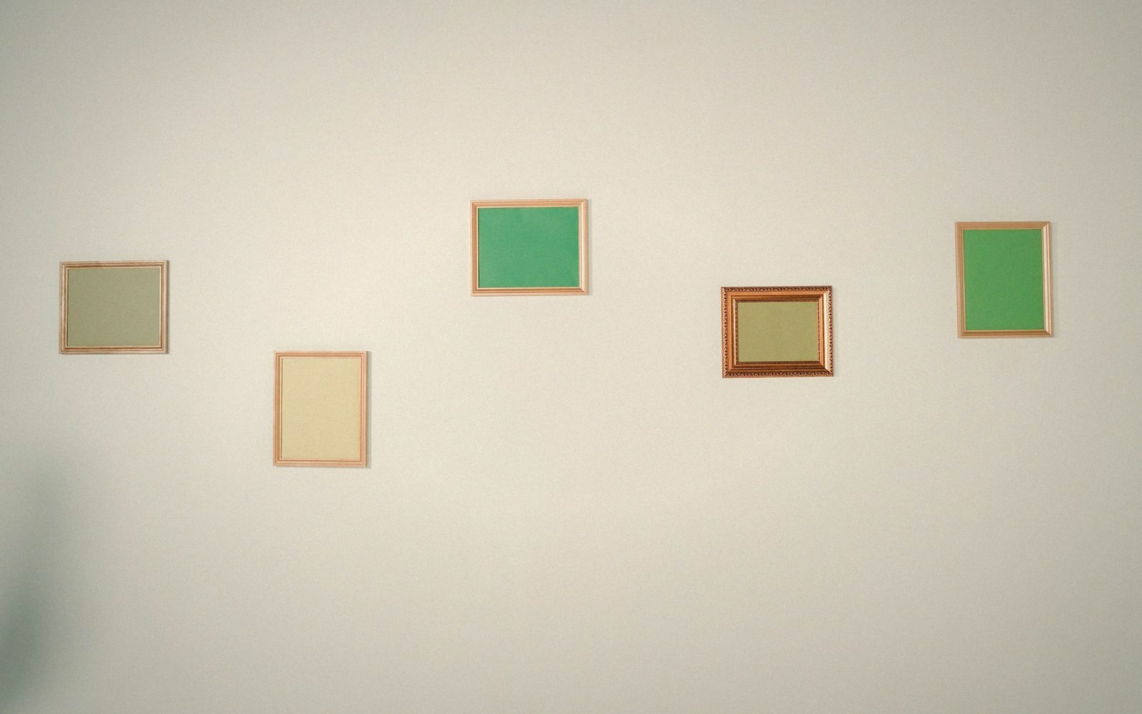 Five empty picture frames with blank colored mats hung in a staggered row on a wall